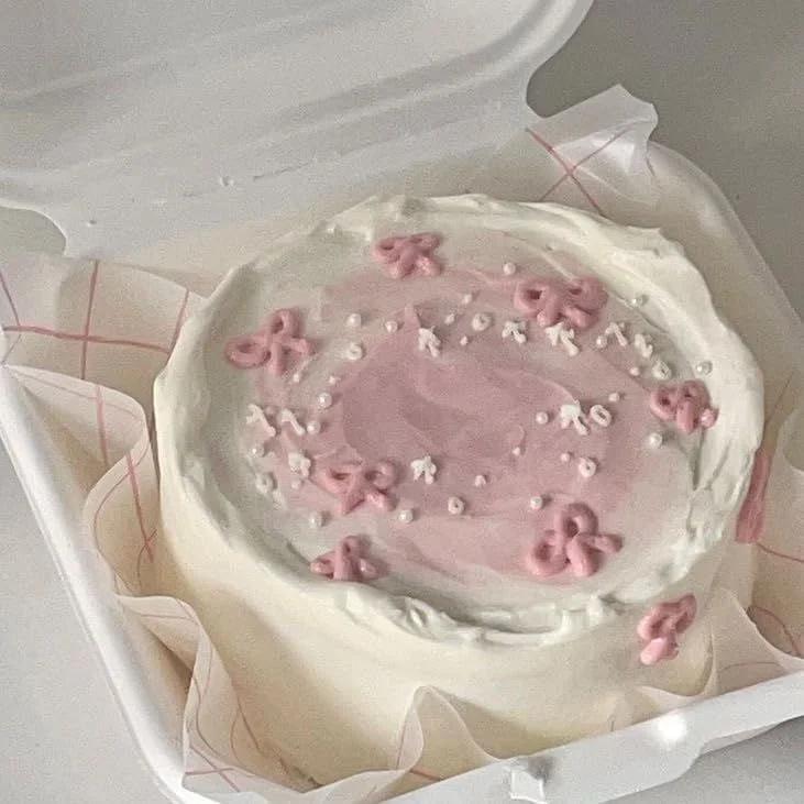 White bento cake with pink palette knife icing, pink icing bows, and white pearl sprinkles in a white container.