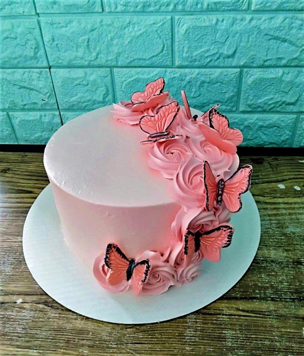 Single tier pink cake decorated with pink icing rosettes and pink butterfly printouts on the side and top.