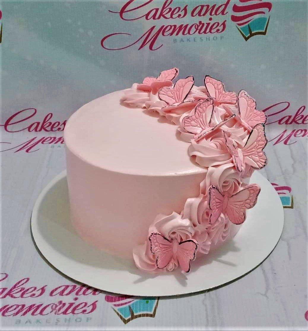 Elegant pink minimalist cake decorated with pink icing rosettes and pink butterfly toppers with black outlines.