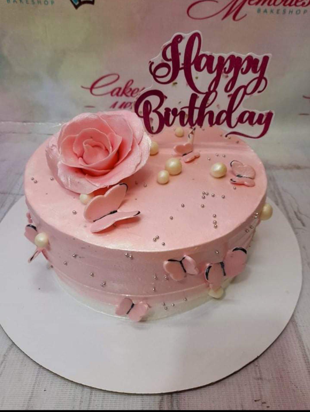 Pink minimalist birthday cake with a large pink fondant rose, pink butterflies, and silver dragees.