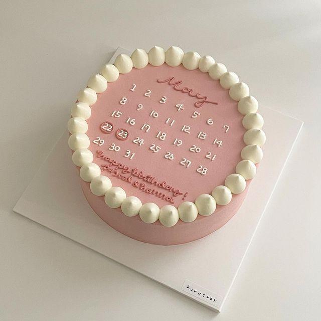 A pink 1 Tier cake featuring a calendar design, white icing text, and white icing dollops.
