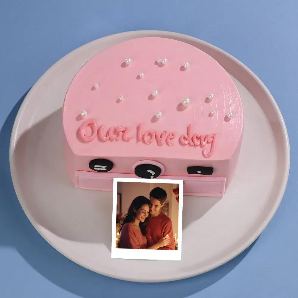 Pink bento cake designed like a vintage camera with a polaroid photo printout and white pearl sprinkles.