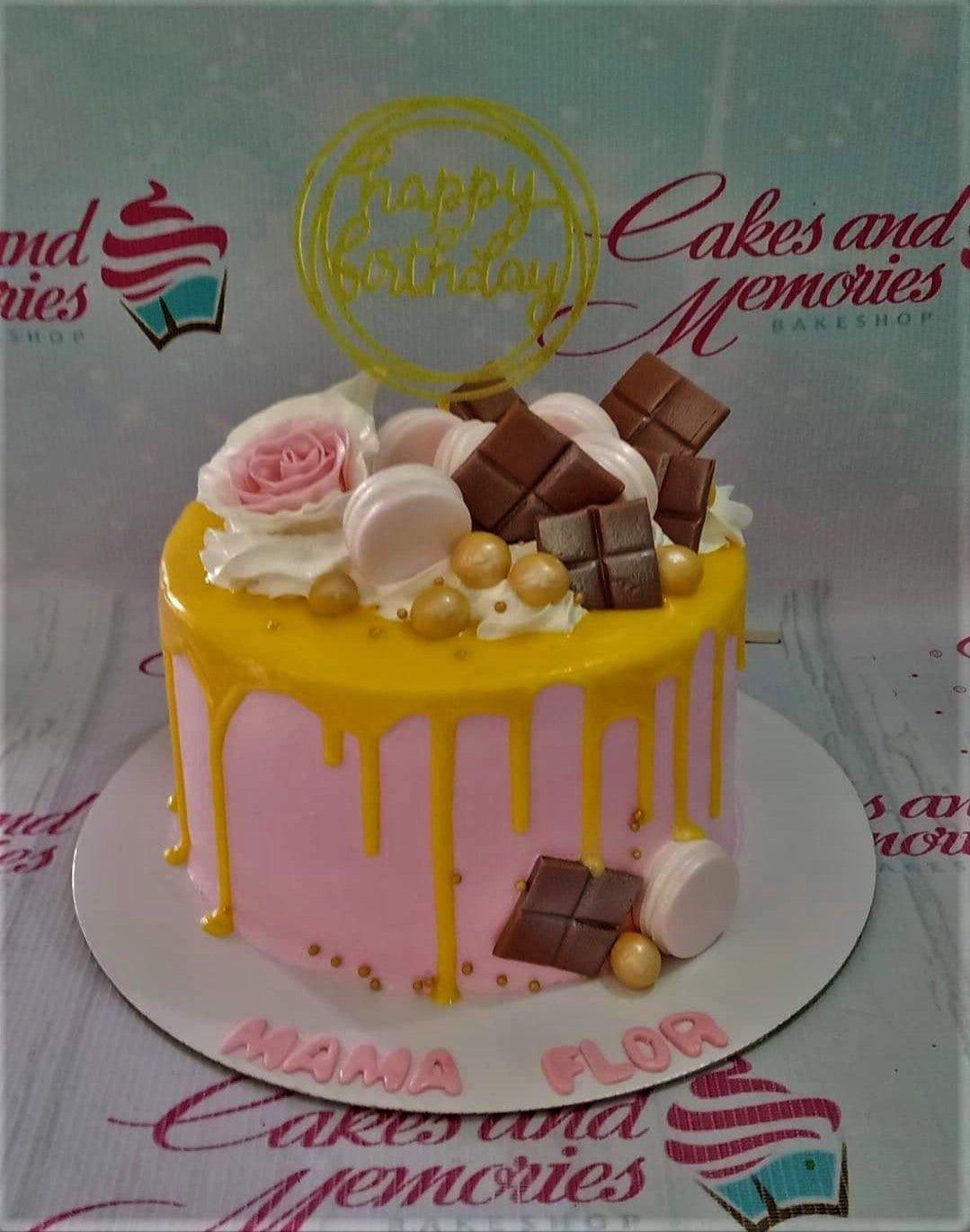 Pink 1-tier cake with yellow drip, chocolate bars, macarons, and a gold Happy Birthday topper.