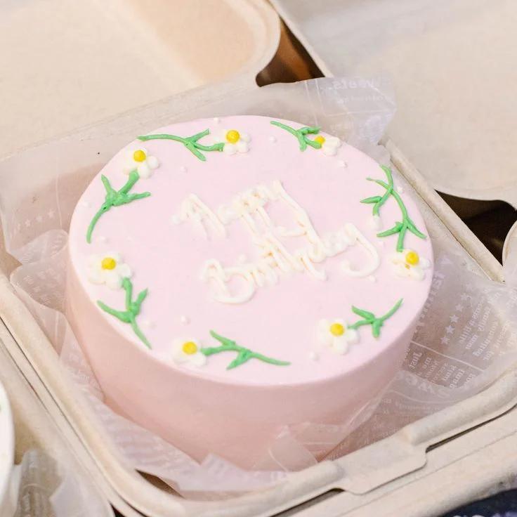 Pink bento cake with white icing flowers and Happy Birthday message in a takeout box.