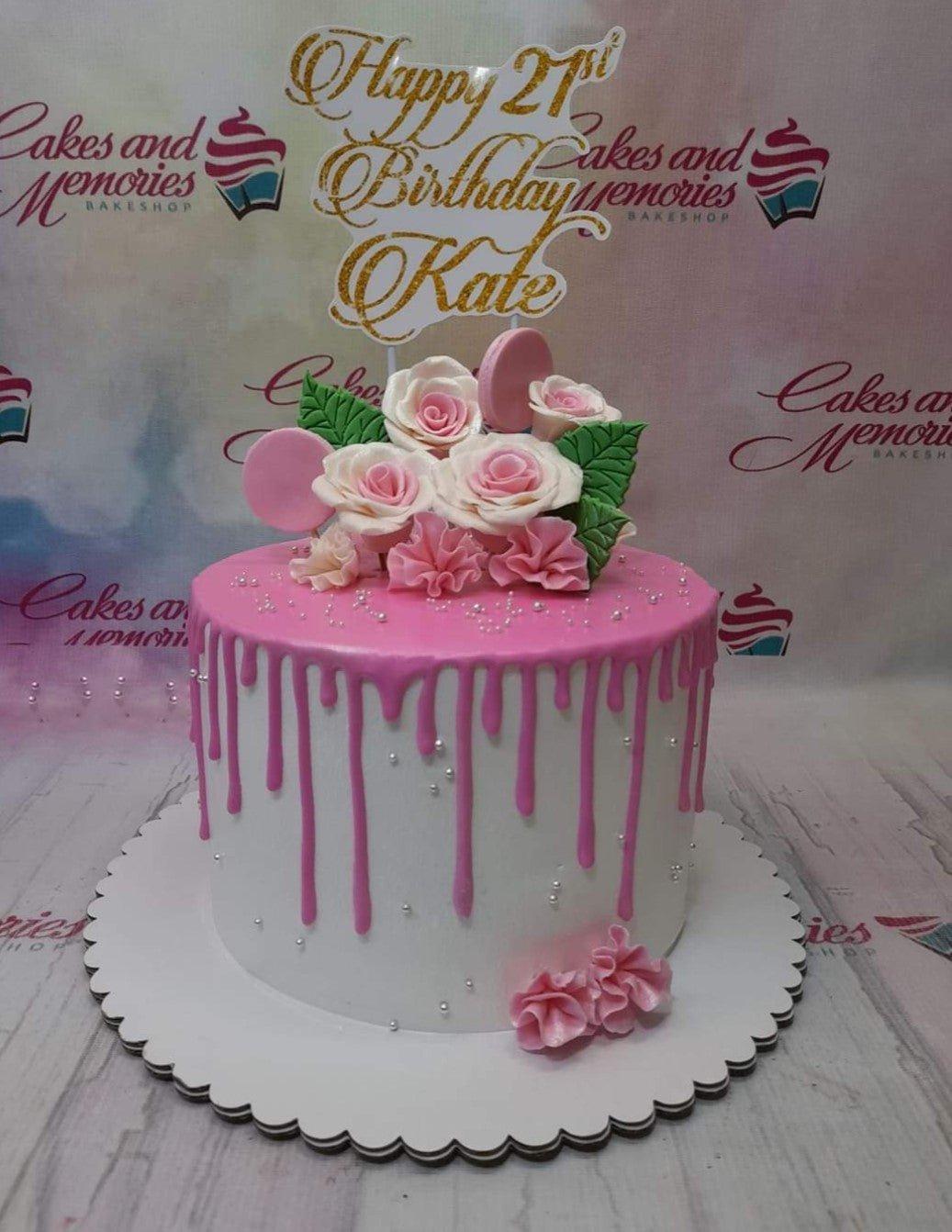 White 1-tier cake with pink drip, pink and white gumpaste roses, and a gold glitter Happy 21st Birthday Kate topper.