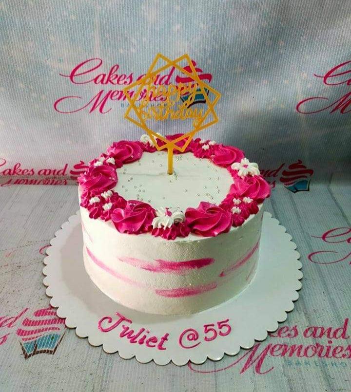 White round cake with pink icing rosettes, silver dragees, and a gold Happy Birthday topper.