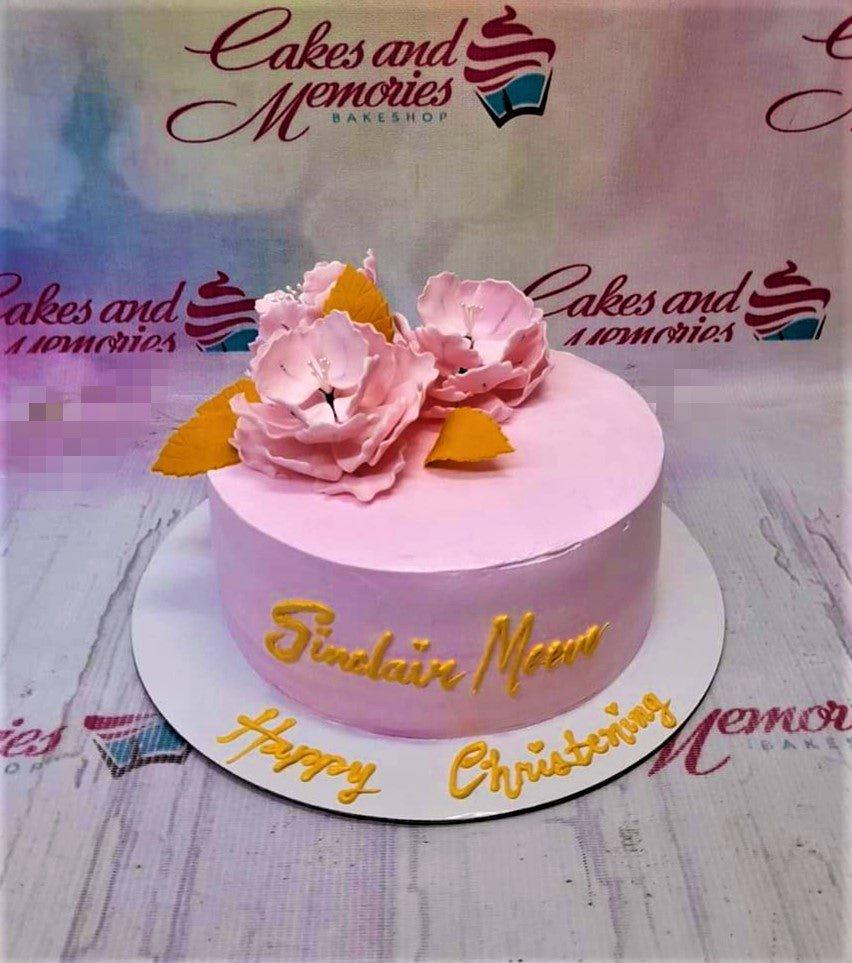 Pink minimalist christening cake with large pink gumpaste flowers and gold leaves on a light pink icing base.