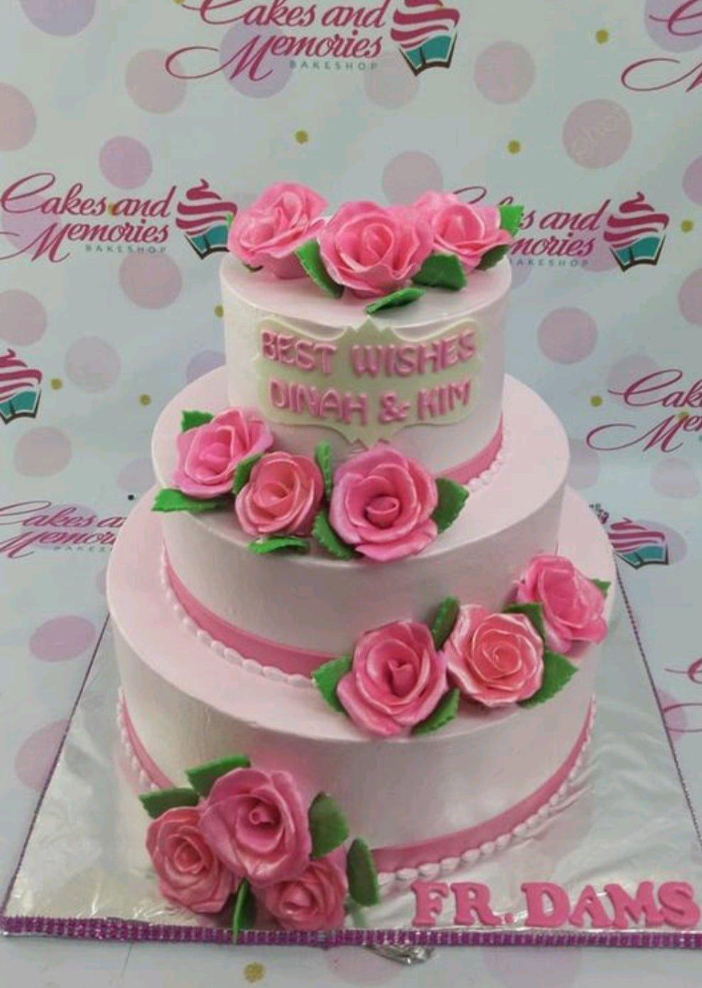 Elegant 3-tier pink floral cake with pink icing roses, green leaves, and a personalized message for Dinah and Kim.