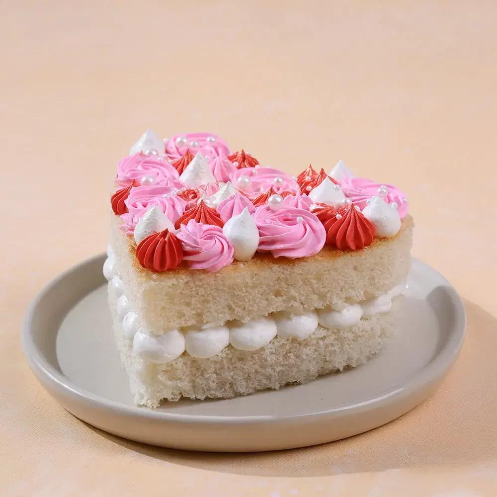 Heart-shaped bento cake with white soft icing filling and pink, red, and white piped rosettes on top decorated with white pearls.