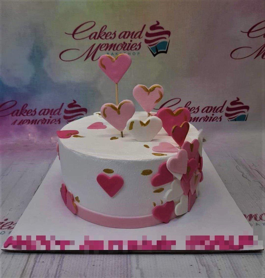 White minimalist cake decorated with pink and white fondant hearts and gold accents.