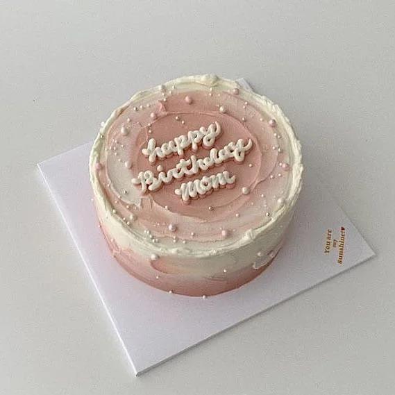 Minimalist pink and white bento cake with palette knife icing texture, white pearls, and 'Happy Birthday Mom' message.