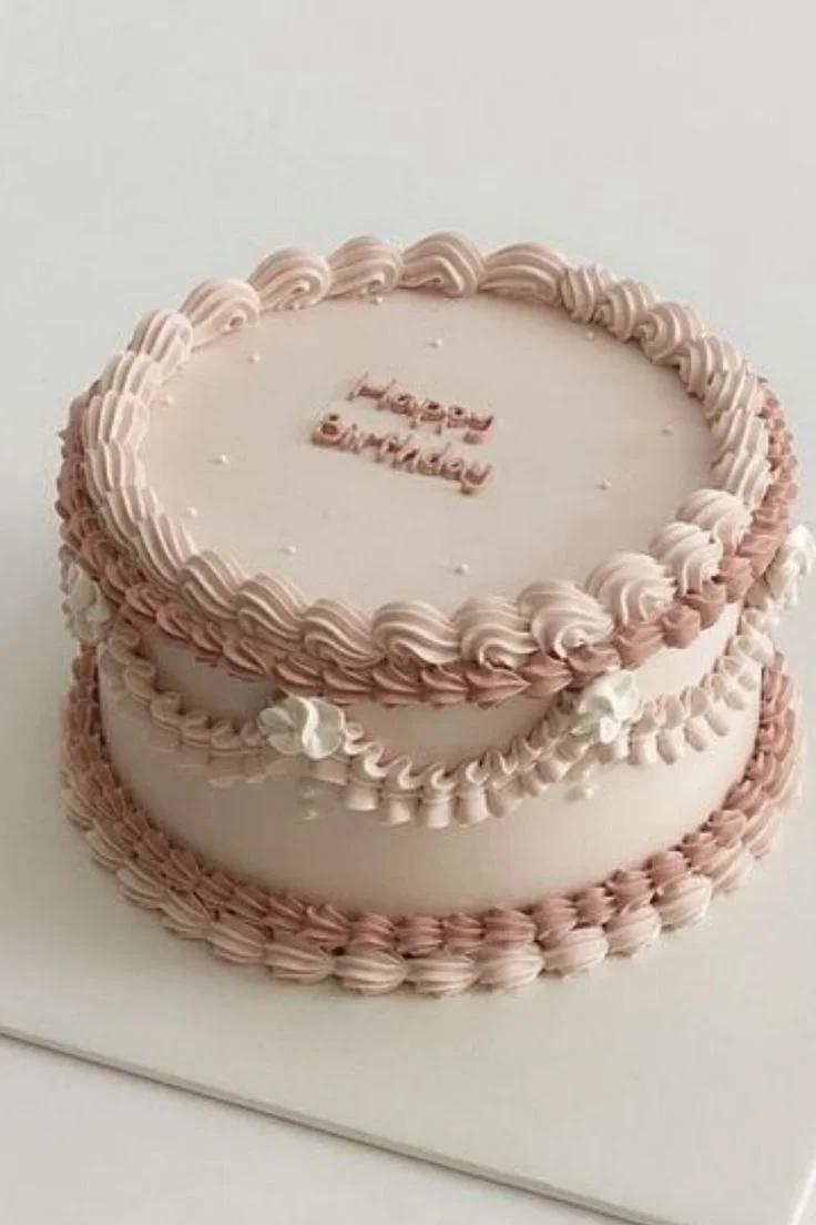 Elegant minimalist pink vintage cake with intricate piped ruffles, white icing flowers, and a Happy Birthday message.