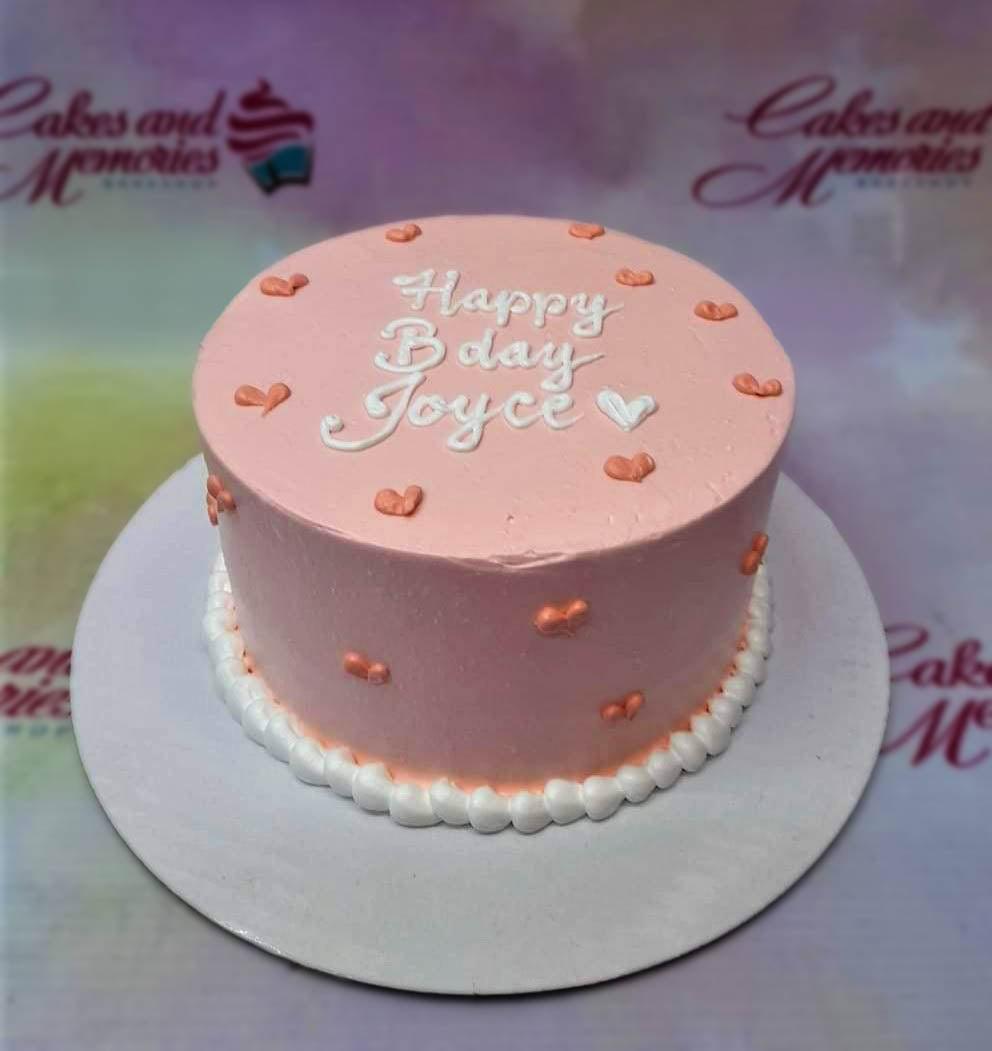 Pink minimalist bento cake with white piped message and small orange heart icing decorations.