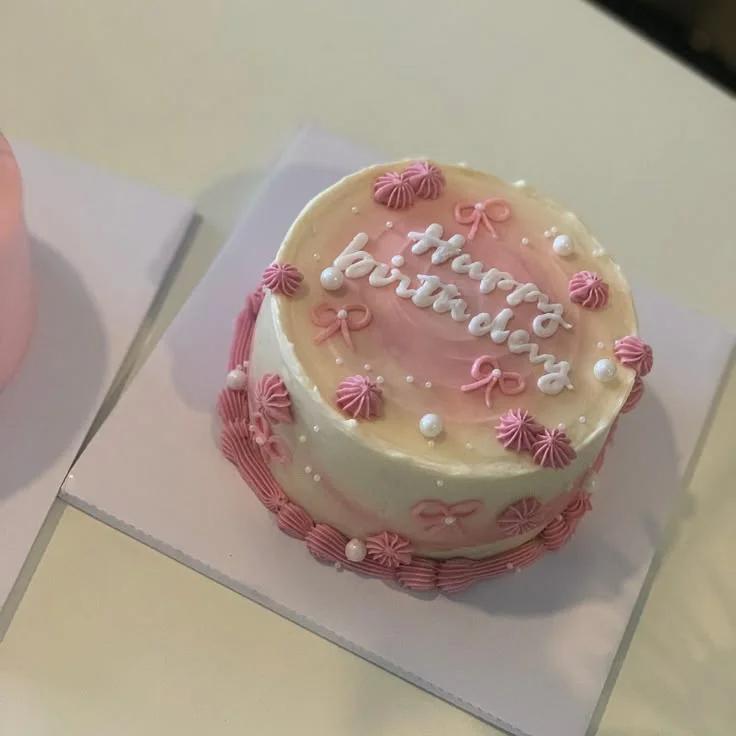 Pink and white bento cake with piped icing rosettes, pink bows, and white pearls featuring a Happy Birthday message.
