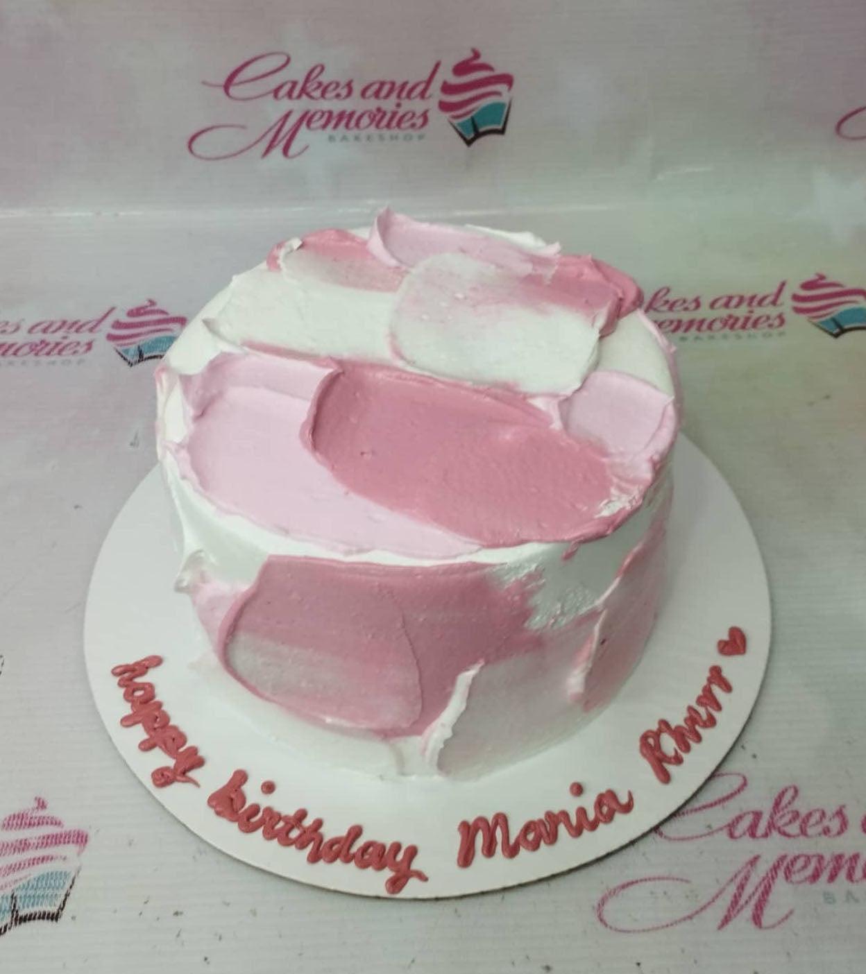 Minimalist white cake with pink and light pink palette knife icing strokes and a birthday message on the base board.