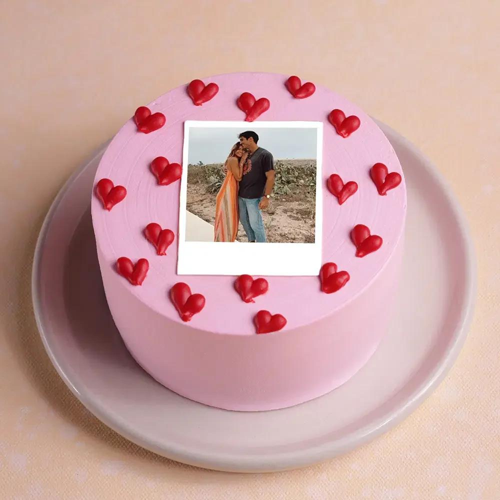 Pink minimalist cake with a polaroid photo printout and red icing hearts on top.