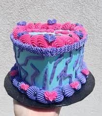 Light blue heart-shaped cake with vibrant hot pink and purple piped icing borders and lightning bolt side decorations.