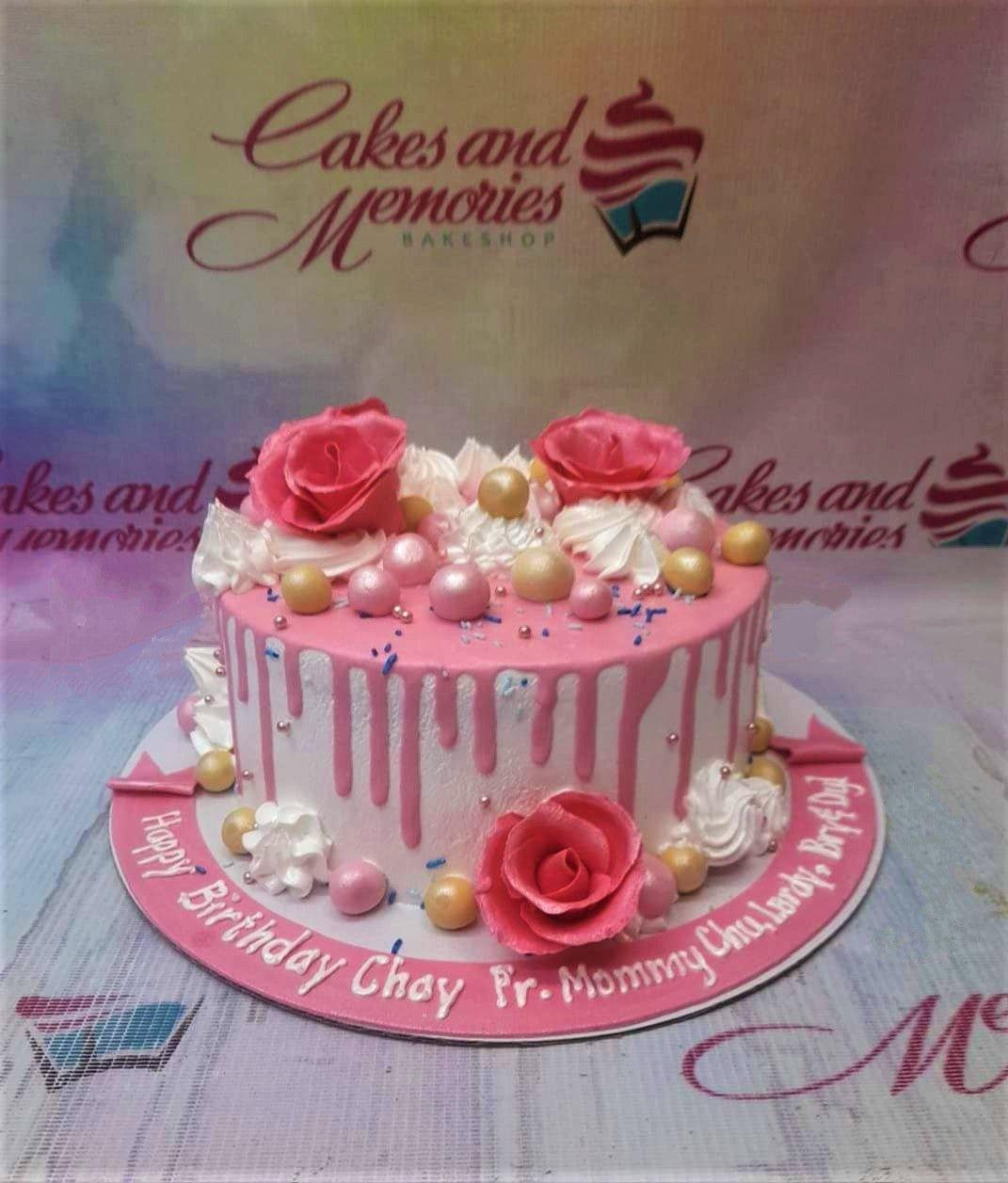Pink and white 1-tier birthday cake with pink icing drip, edible roses, and gold and pink spheres on a pink fondant base board.