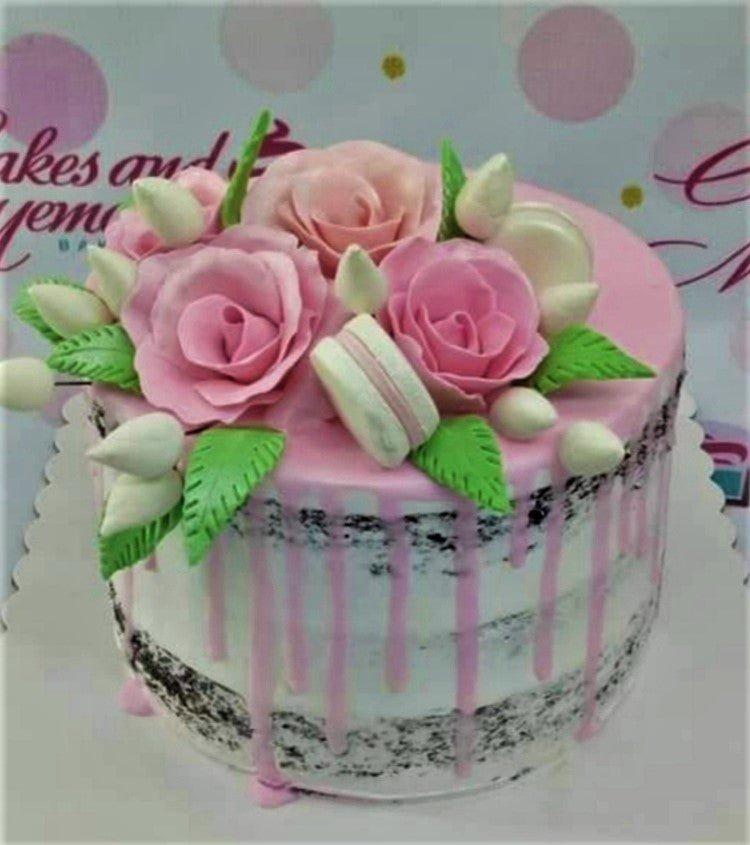 Pink semi-naked cake with pink gumpaste roses, white macarons, and green leaves on top with pink icing drips.