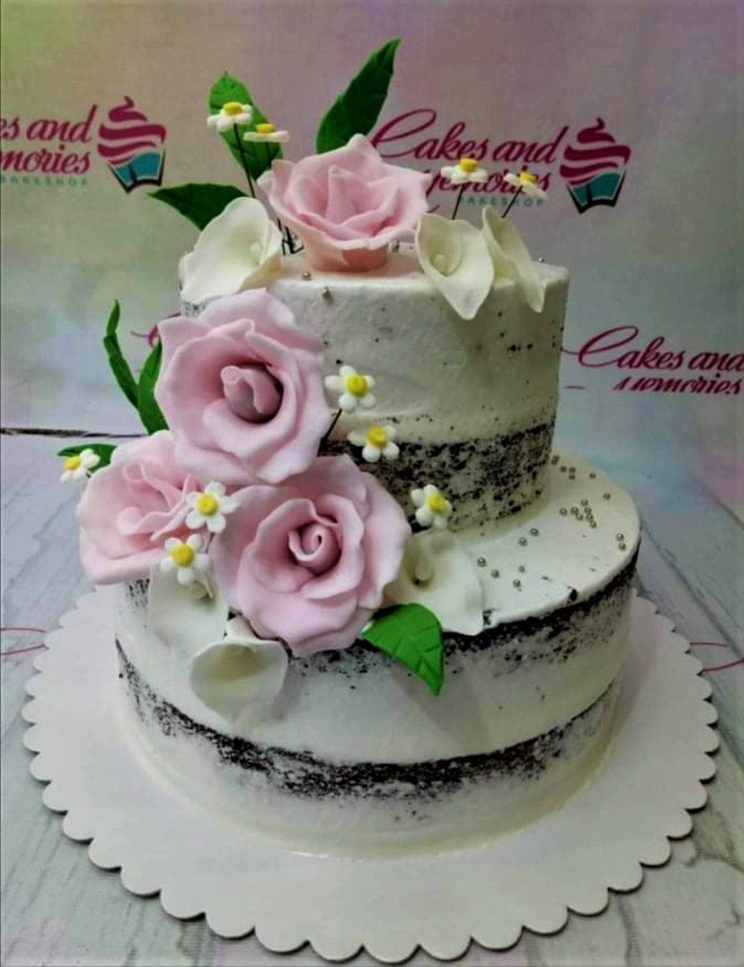 Two-tier semi-naked chocolate cake decorated with large pink gumpaste roses, white calla lilies, and silver dragees.