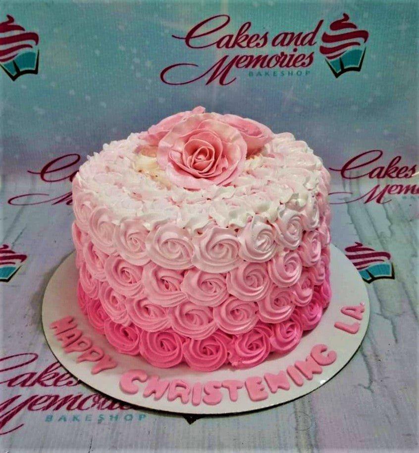 Pink ombre rosette cake with a large pink fondant rose on top and a christening message on the base board.