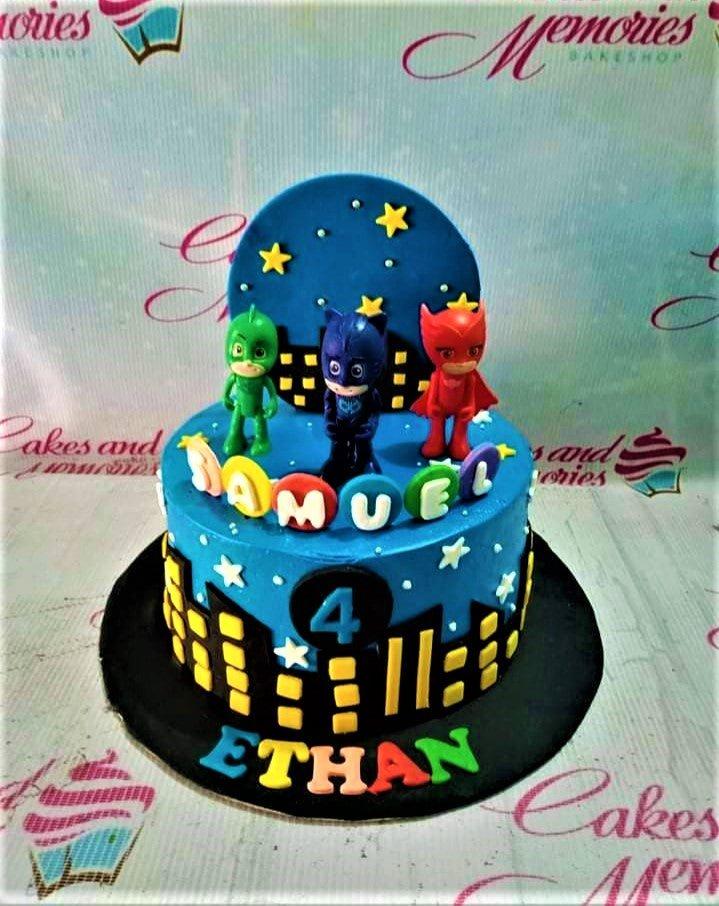 Blue PJ Masks themed birthday cake with 3D character figures, a city skyline, and yellow stars.