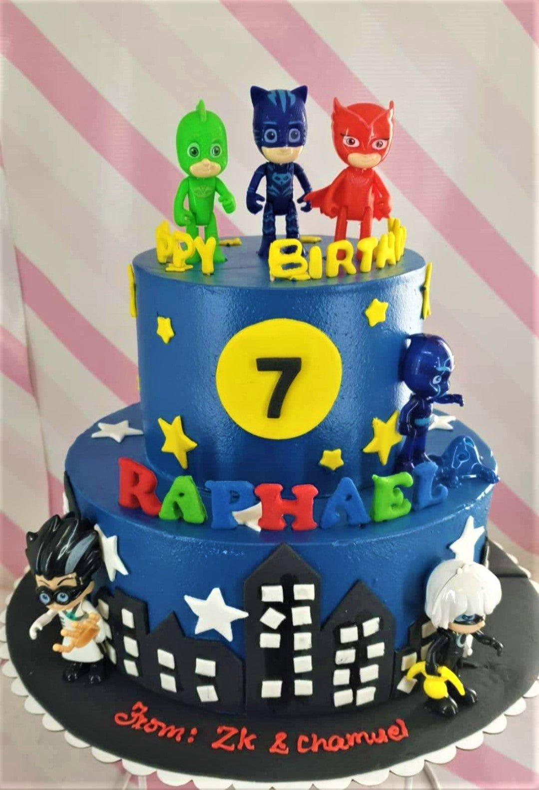 Blue 2-tier PJ Masks birthday cake with 3D character figures, yellow stars, and a black fondant city skyline.