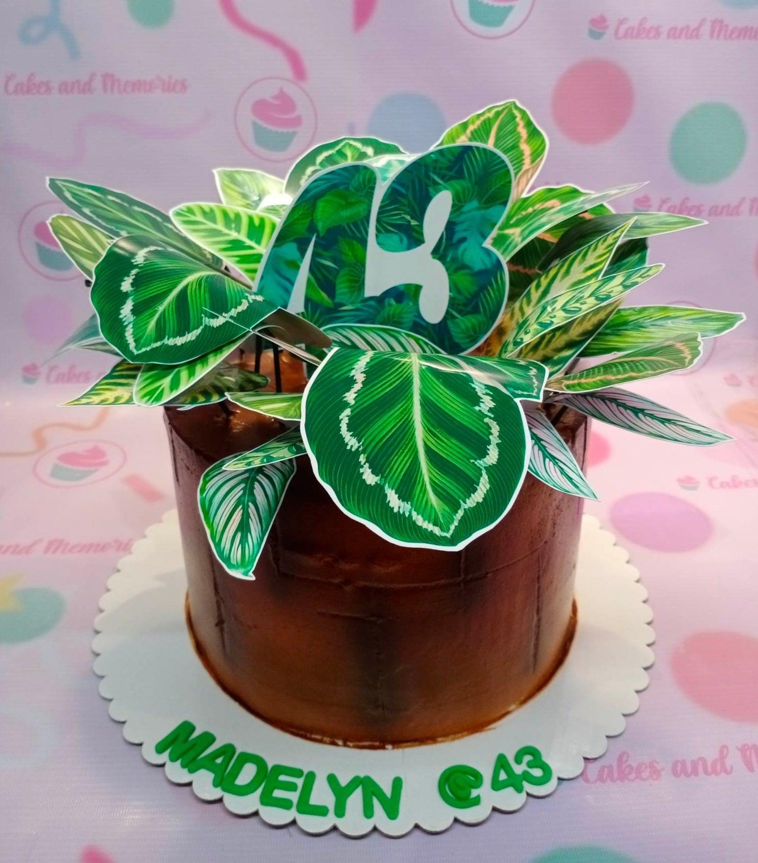 Single tier brown cake with a lush arrangement of green leaf printouts and a large number 43 topper on top.