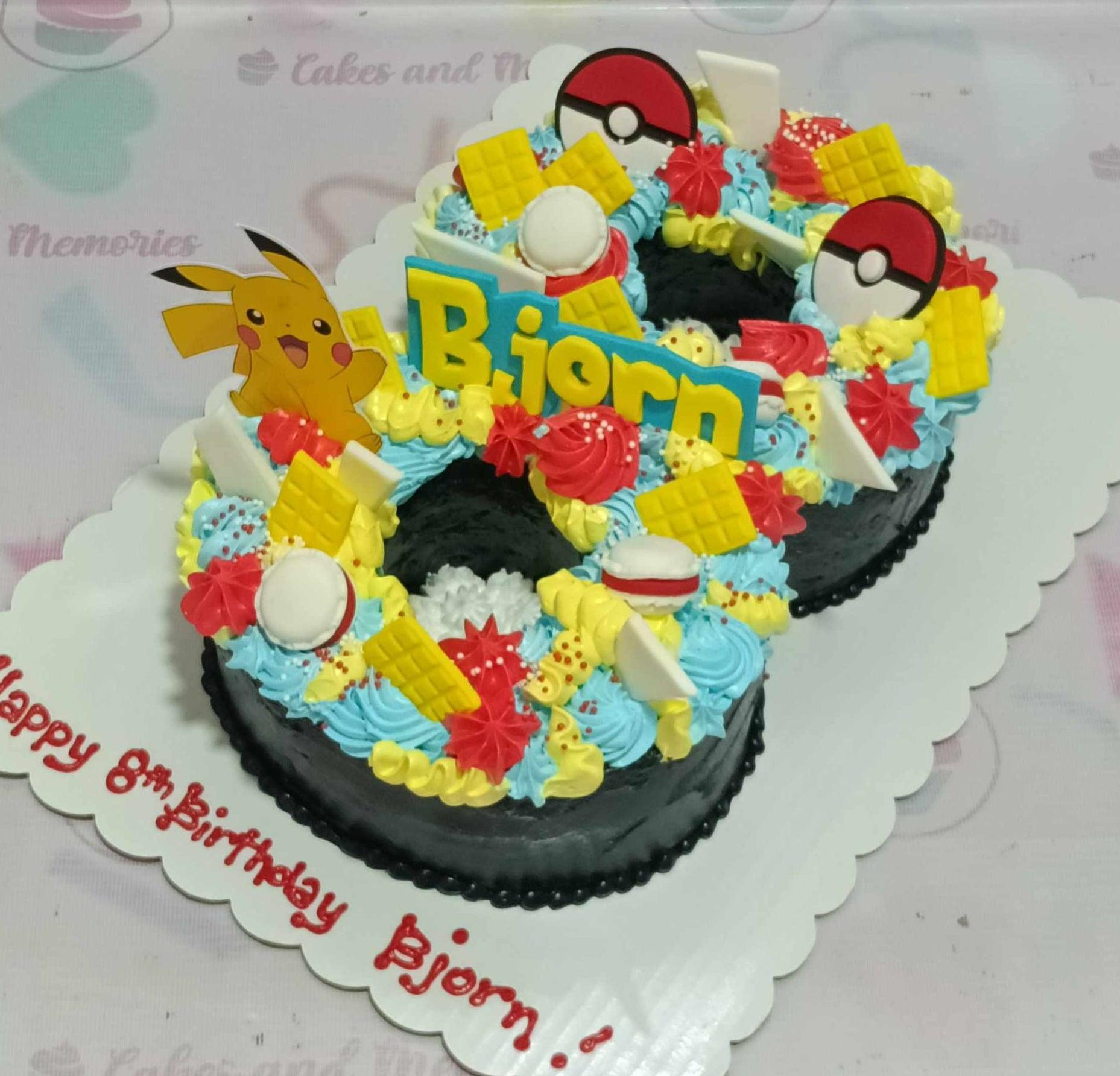 Number 8 shaped Pokemon themed cake with Pikachu and Pokeball toppers, blue and yellow icing rosettes, and a birthday message on the board.