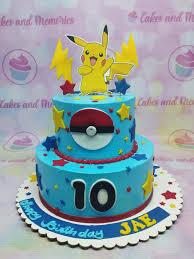 A light blue 2-tier cake featuring Pikachu and Pokeball printouts, yellow lightning bolts, colorful stars, and a red beaded icing border.