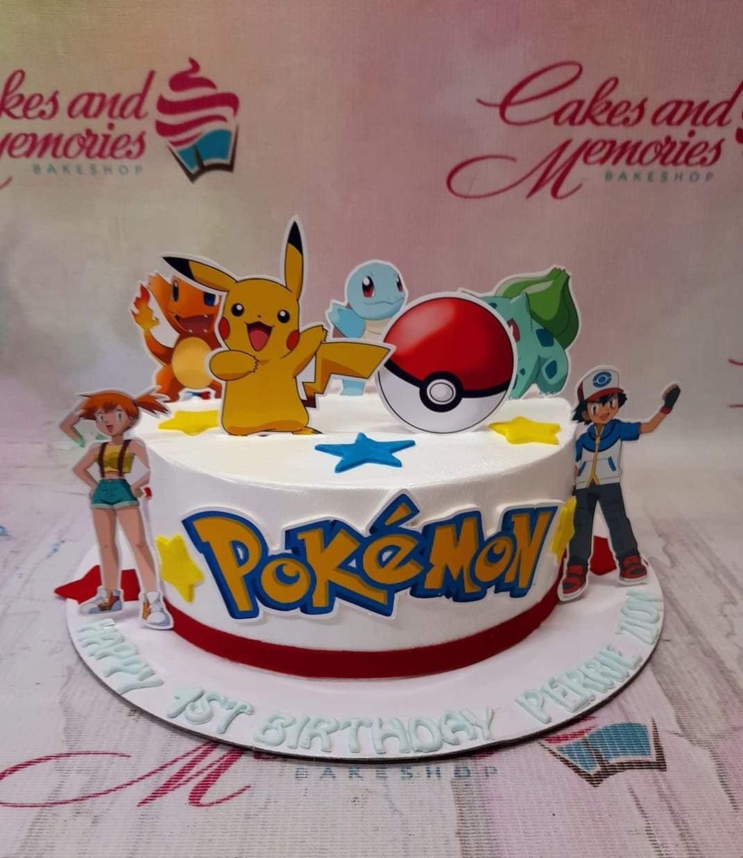 White Pokemon themed birthday cake with Pikachu, Charmander, Squirtle, Bulbasaur, and Ash Ketchum printout toppers and a large Pokemon logo.