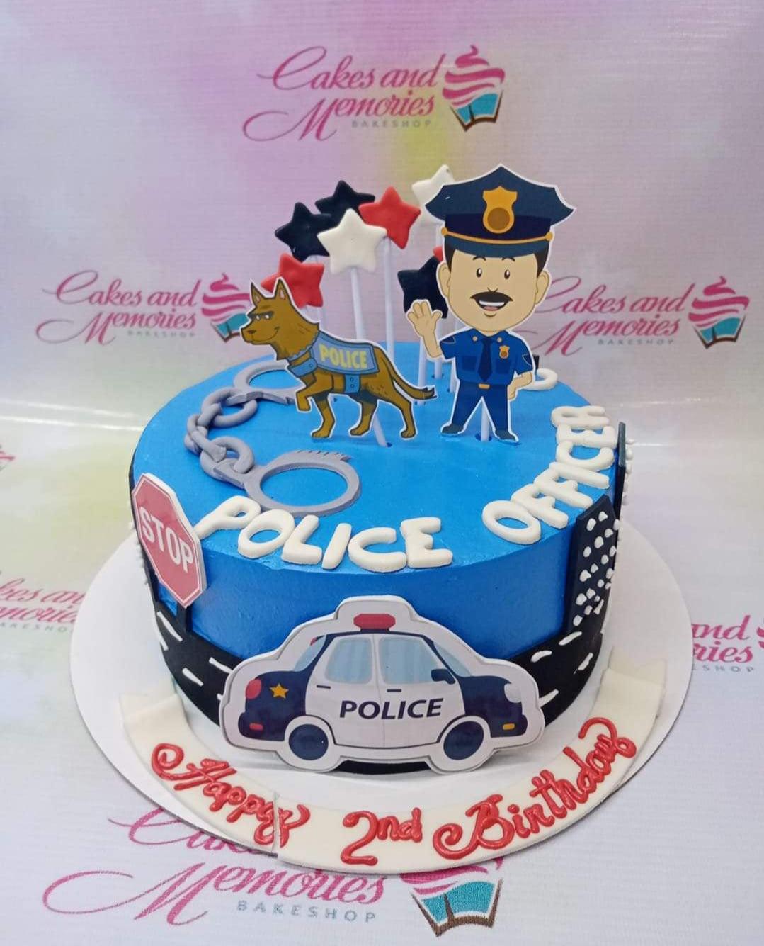 Blue police officer themed birthday cake with police car, officer, and K9 printouts on a black road base.