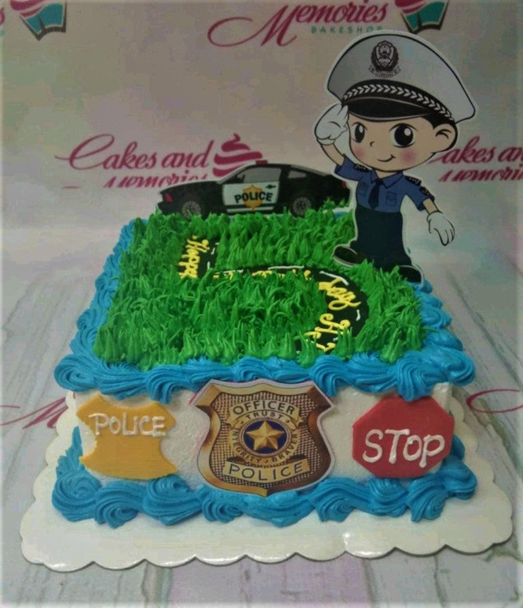 Square police themed birthday cake with green grass icing, a police officer cutout, and a police car topper.
