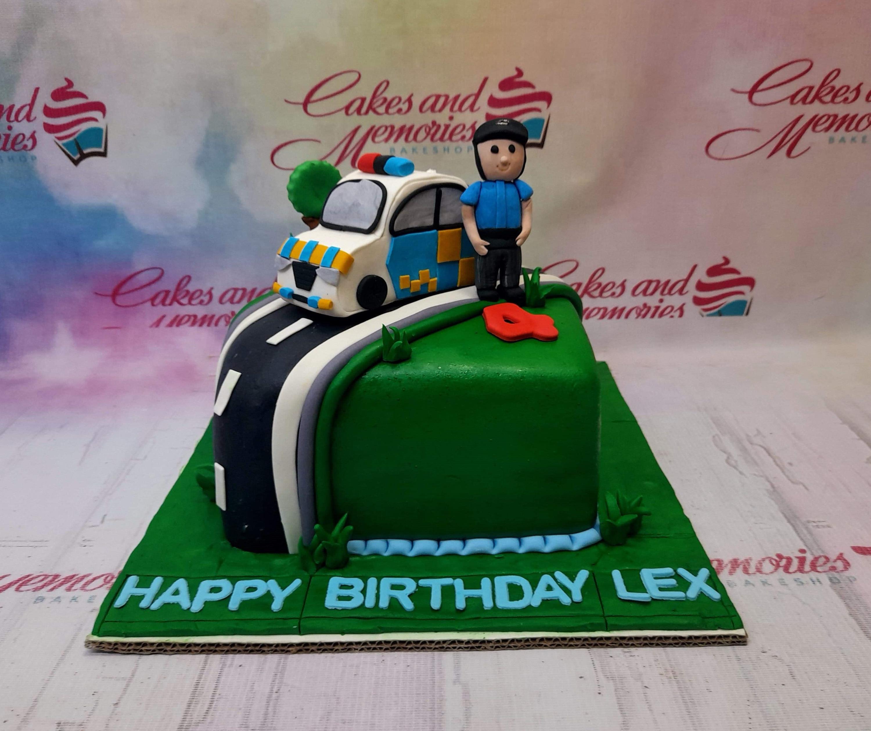 Green square fondant police themed cake with a 3D police car, officer figure, and road design on a green base board.