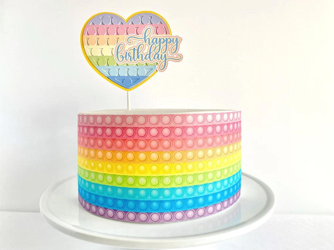 Rainbow pop-it themed birthday cake with a heart-shaped topper and colorful horizontal stripes.