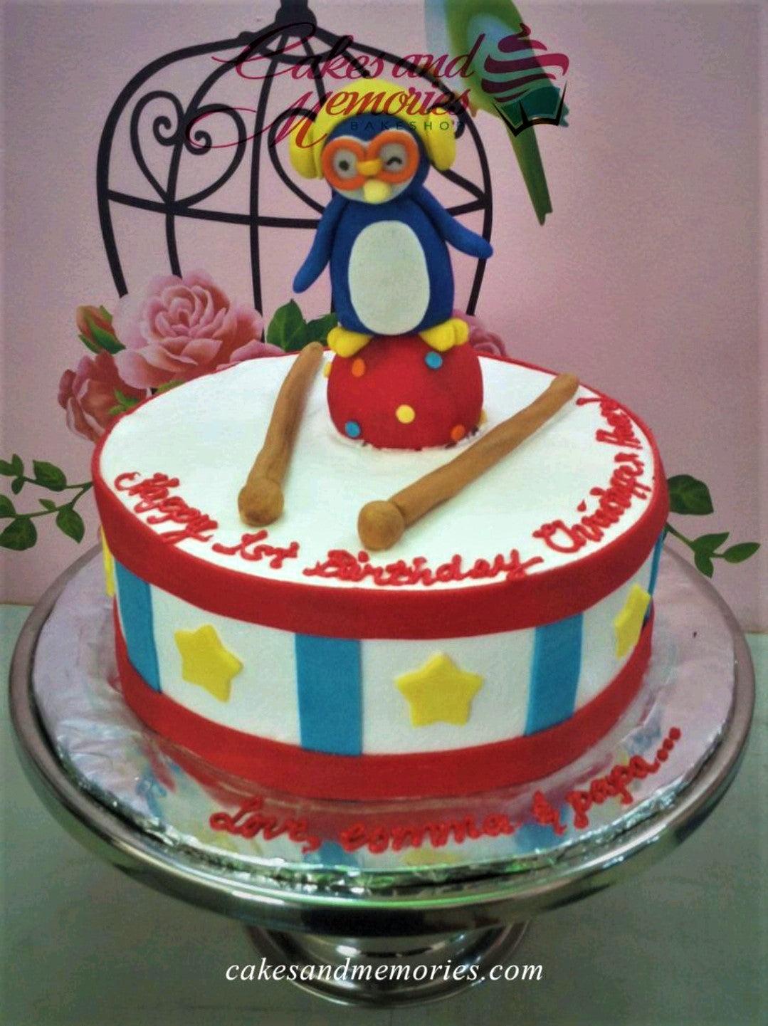 Pororo the Little Penguin themed drum cake with a 3D penguin figure, drumsticks, and red and blue stripes.