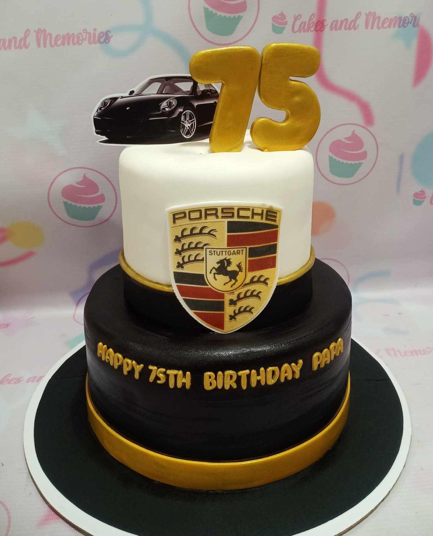 Two-tier Porsche themed birthday cake in black and white with gold accents and a car topper.