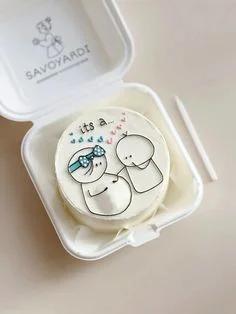White bento cake with a minimalist doodle of a pregnant couple and blue and pink hearts in a takeout box.