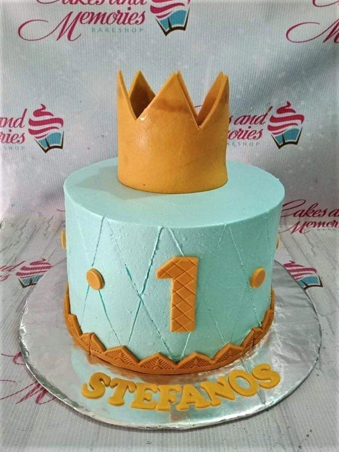 Light blue 1-tier birthday cake with a large gold crown topper, quilted icing pattern, and gold number one.