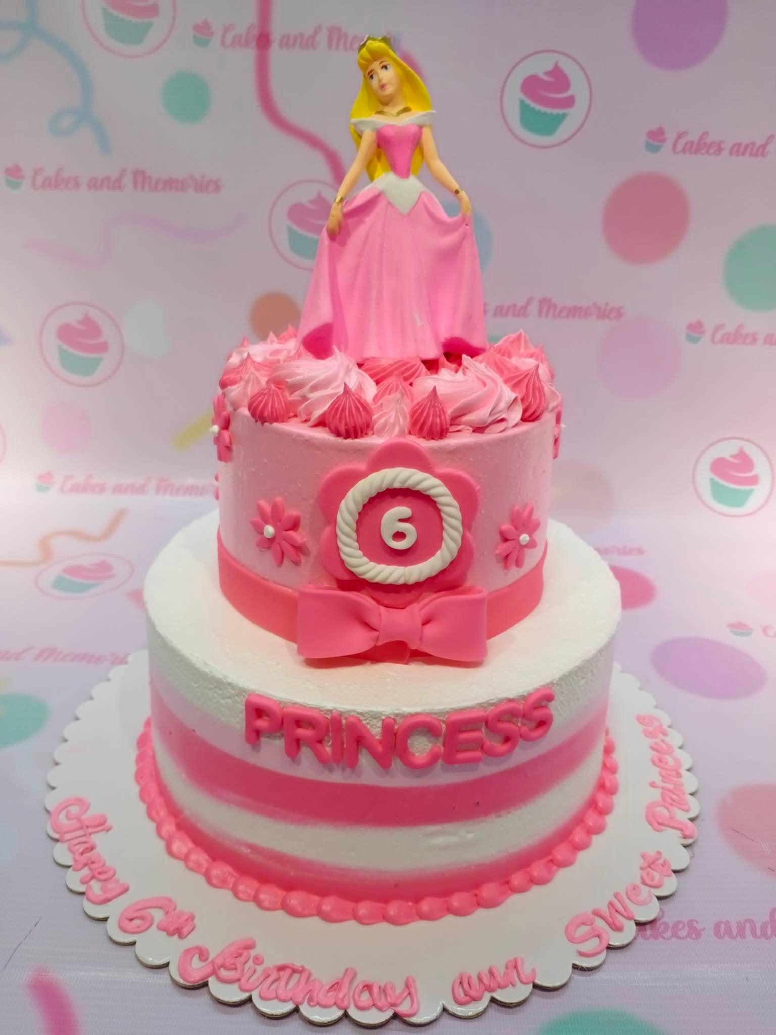 Two-tier pink and white princess birthday cake featuring a 3D Aurora figurine, pink fondant bow, and striped icing design.