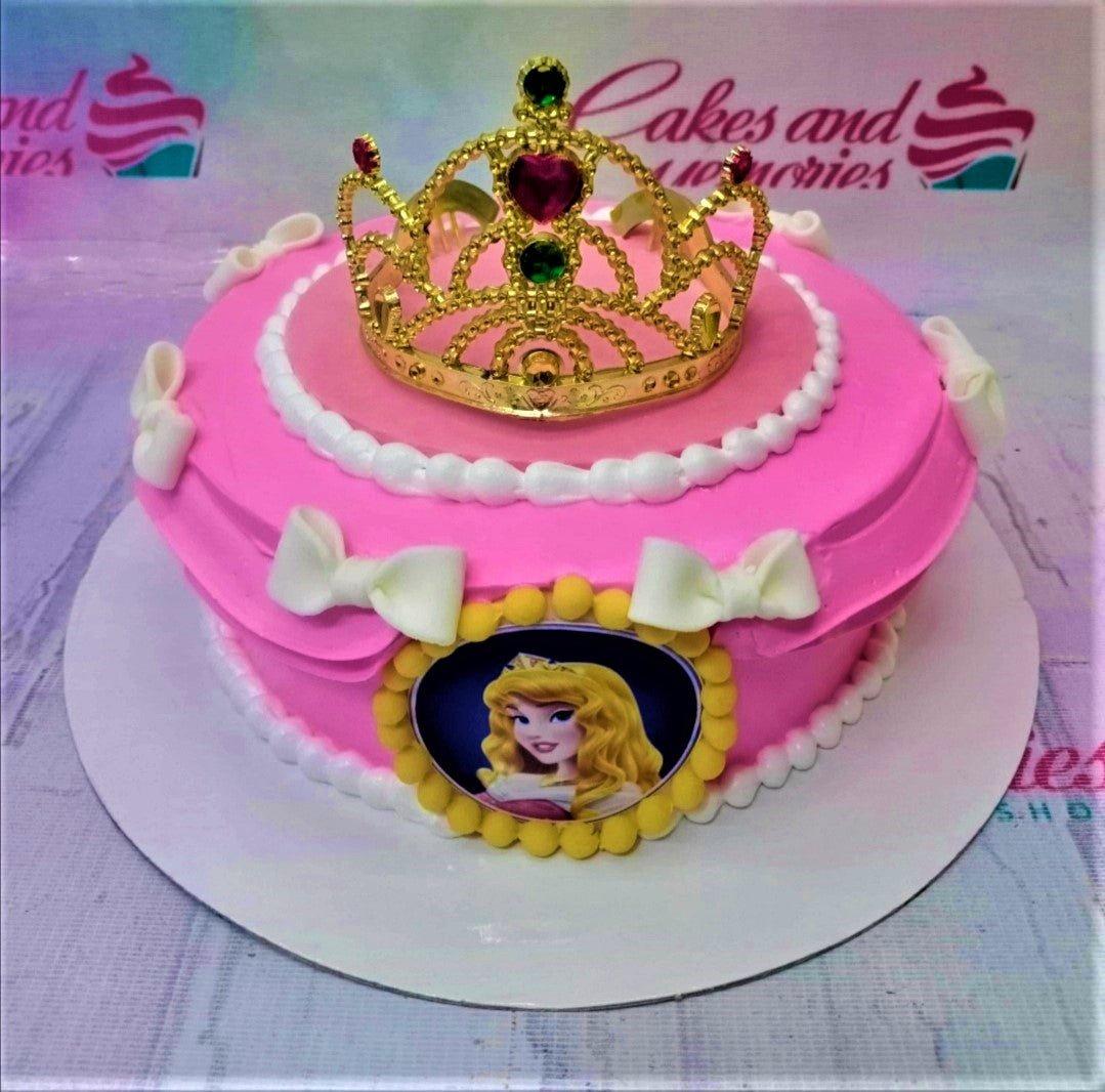 Pink princess themed cake with a gold crown topper, white fondant bows, and a Sleeping Beauty Aurora printout.