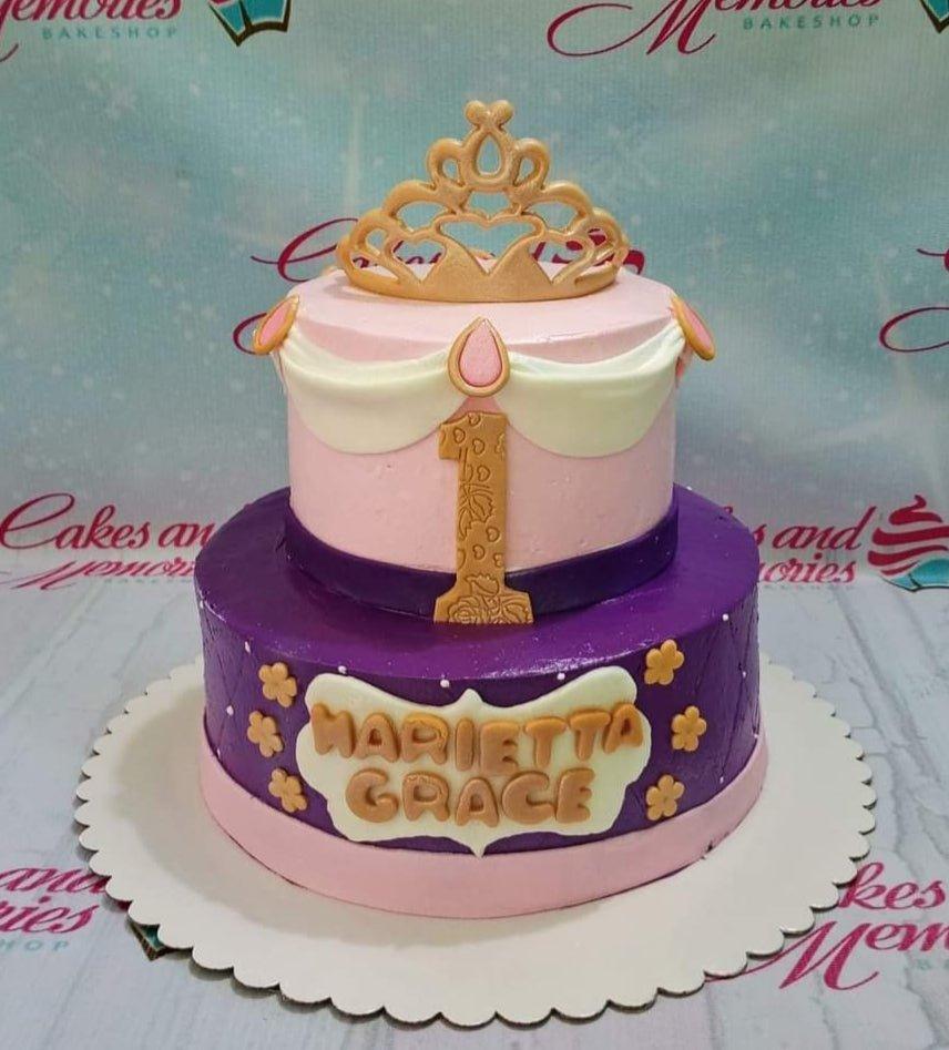 Two-tier pink and purple princess cake with a gold crown topper, white drapes, and gold floral accents.