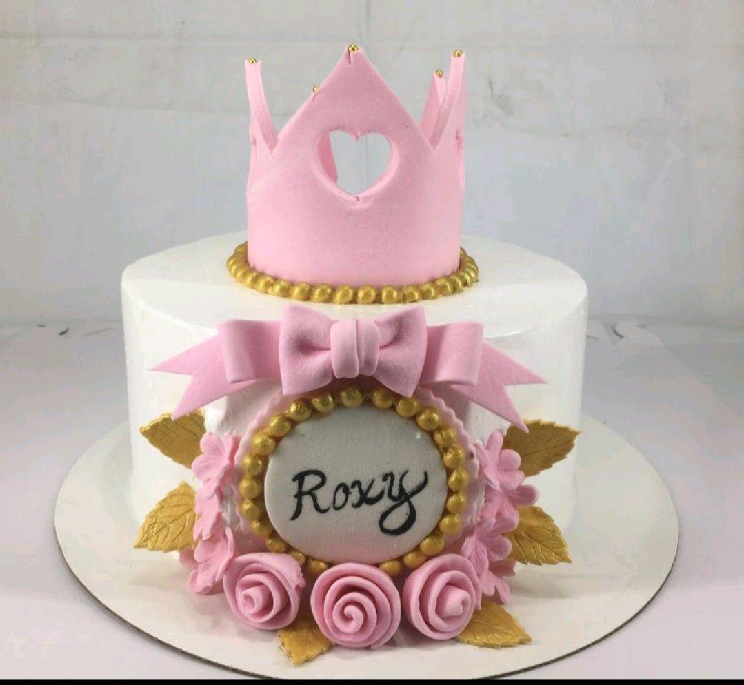 White princess cake with a pink fondant crown, pink bow, and pink roses with gold leaves.