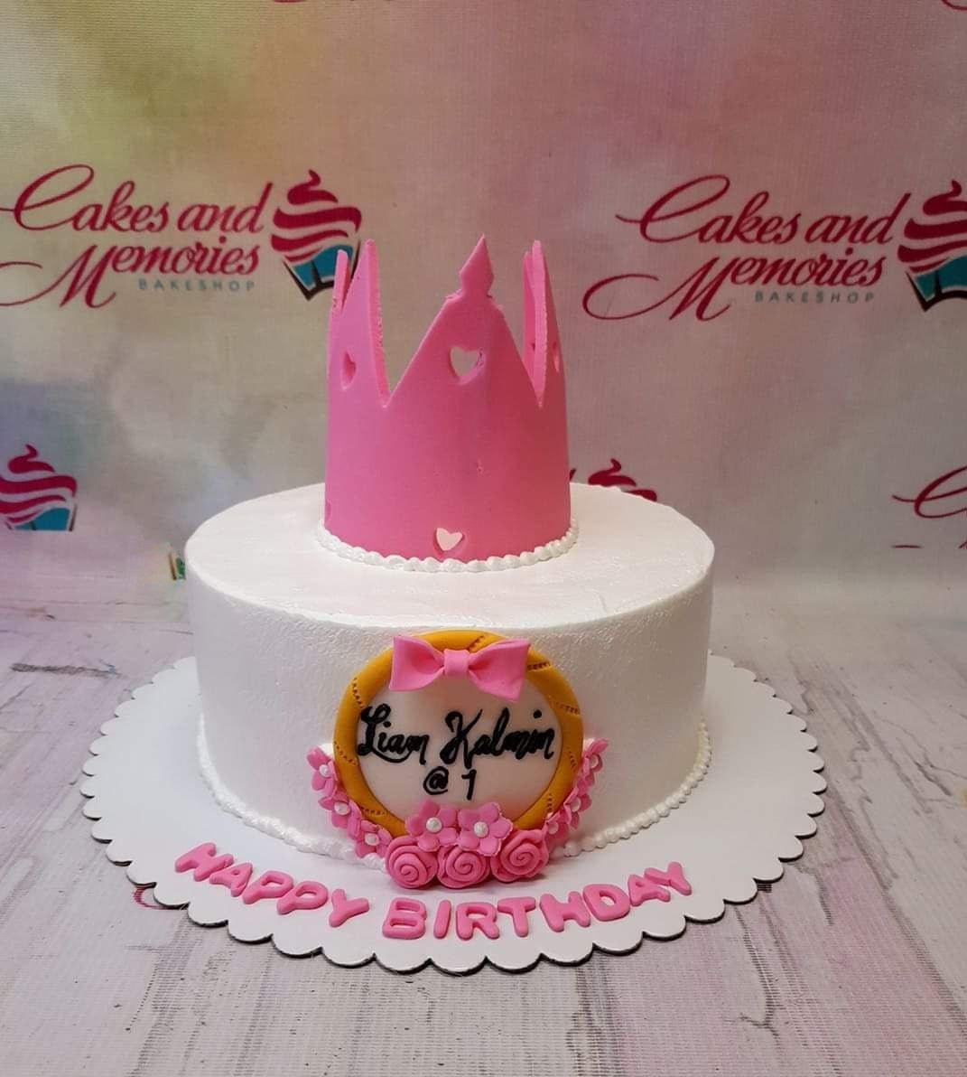 White 1-tier princess birthday cake with a large pink fondant crown and a personalized name plaque with pink flowers.