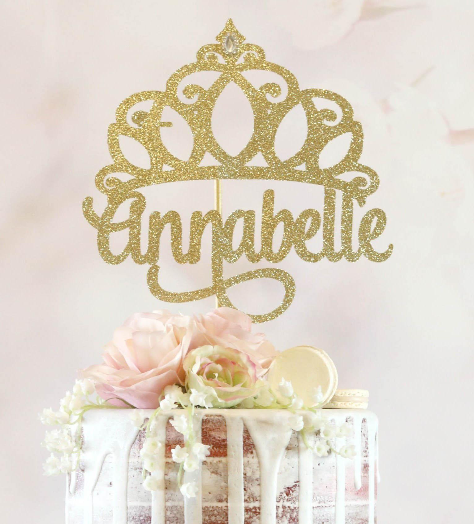 Semi-naked 1-tier cake with white chocolate drip, pink roses, white macarons, and a gold glitter crown name topper.