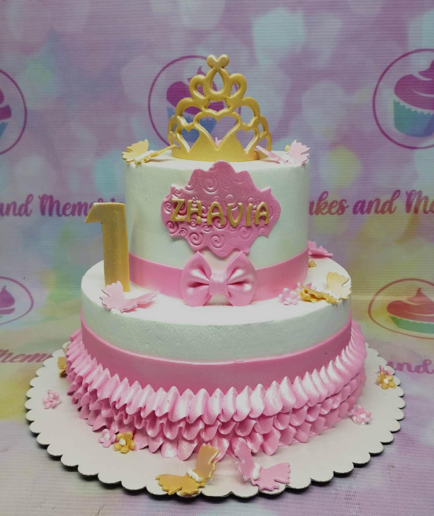 Two-tier white and pink princess cake with a gold crown topper, pink bow, and butterfly accents.