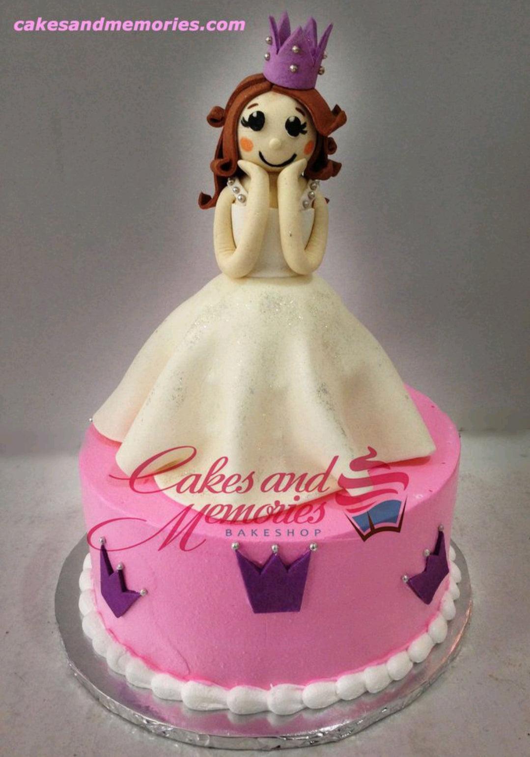 Pink princess doll cake with a large white fondant dress topper and purple crown accents.
