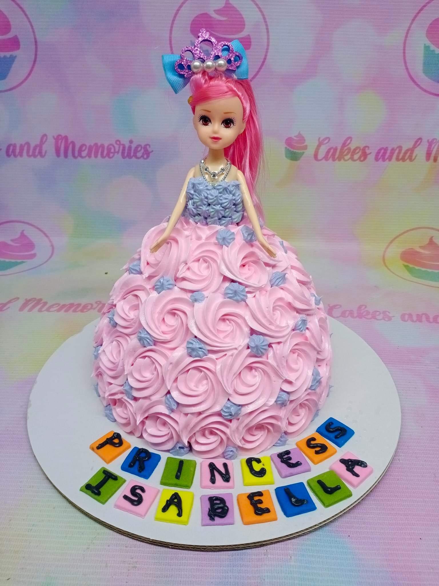 Pink doll cake with a pink-haired doll topper wearing a blue crown and a dress made of pink and blue icing rosettes.
