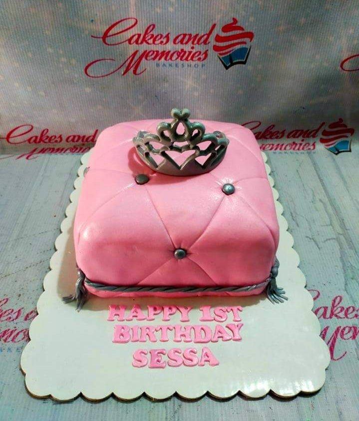 Pink quilted pillow cake with a silver crown topper and silver tassels for a 1st birthday celebration.