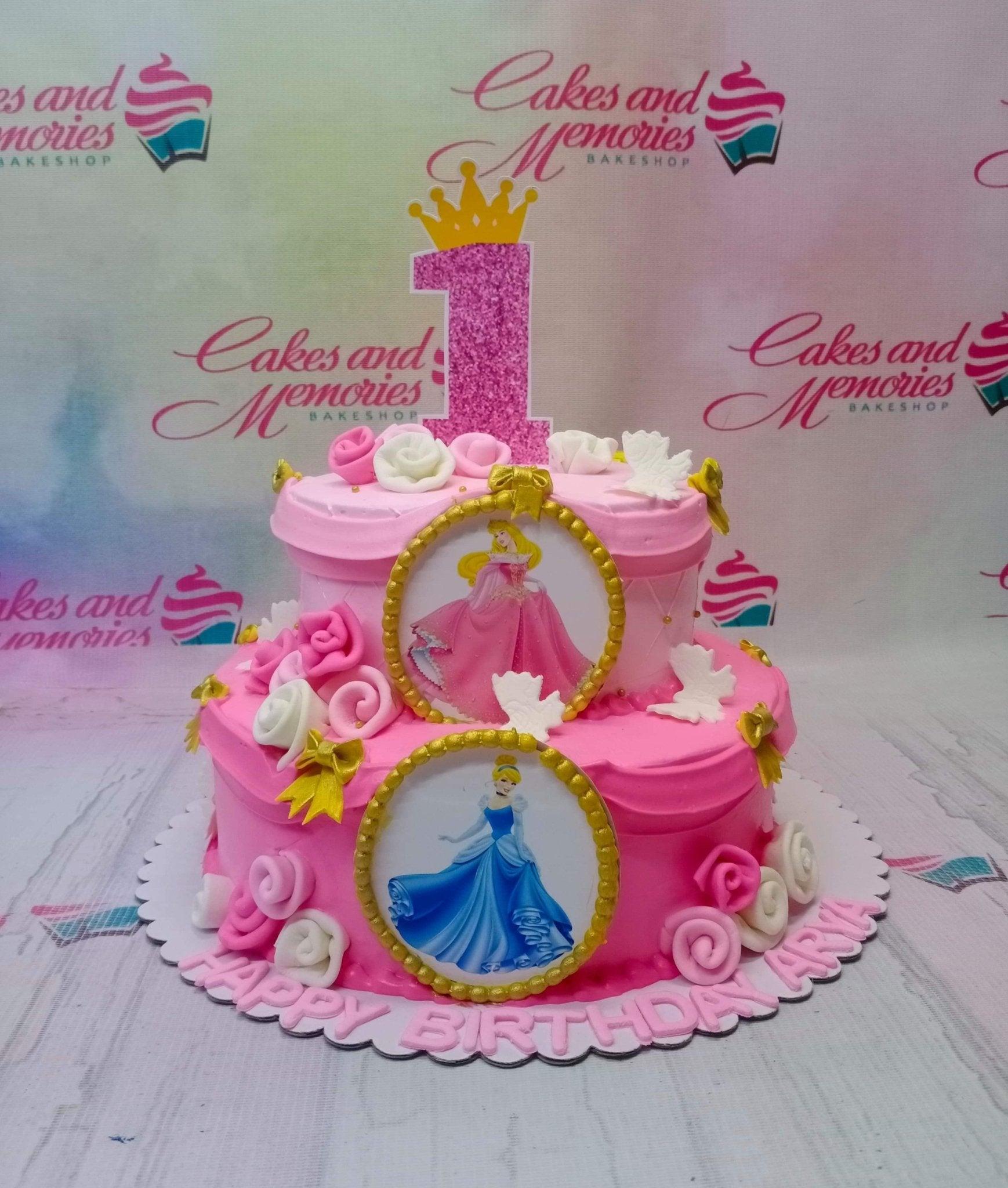 Pink 2-tier Disney Princess birthday cake with Aurora and Cinderella printouts, fondant roses, and a glittery number one topper.